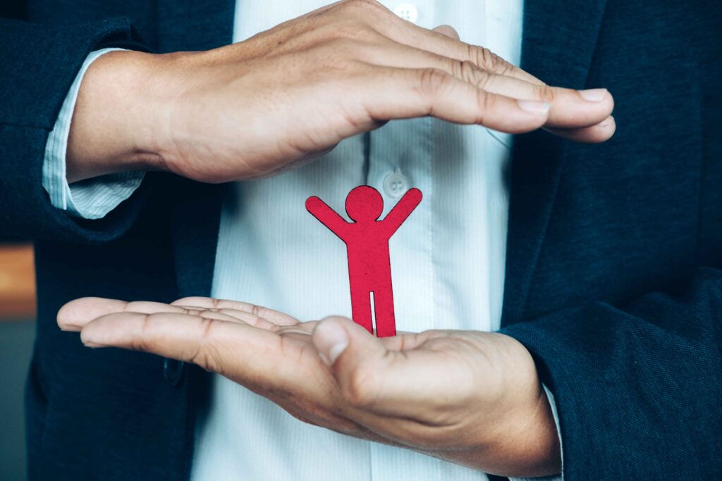 Close-up of a person holding a cardboard cut human figure symbolizing employee protection and security.

